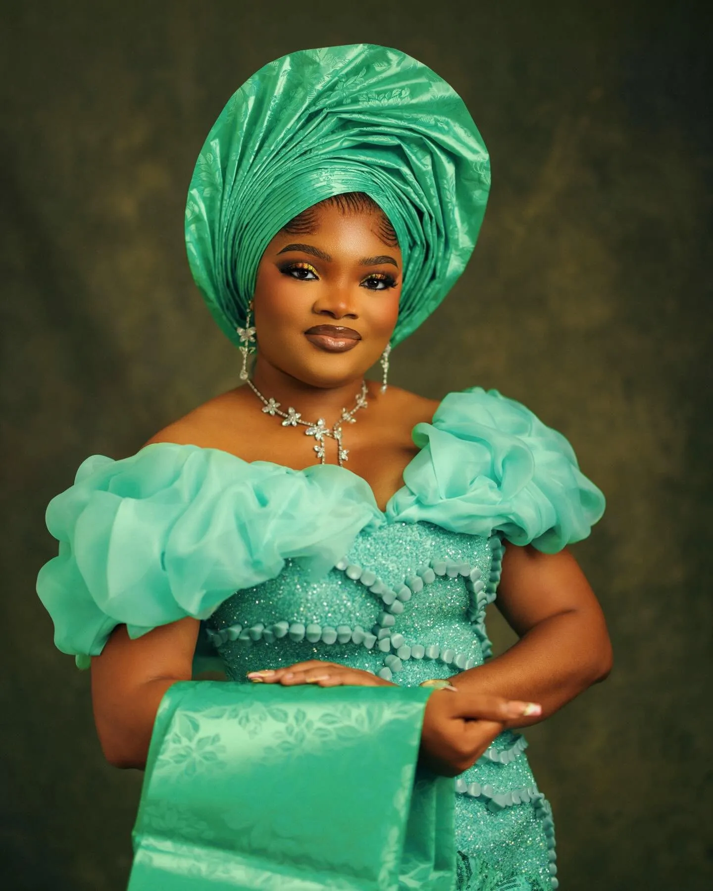 Woman in a jade gele and ruffled off-shoulder gown, holding a clutch