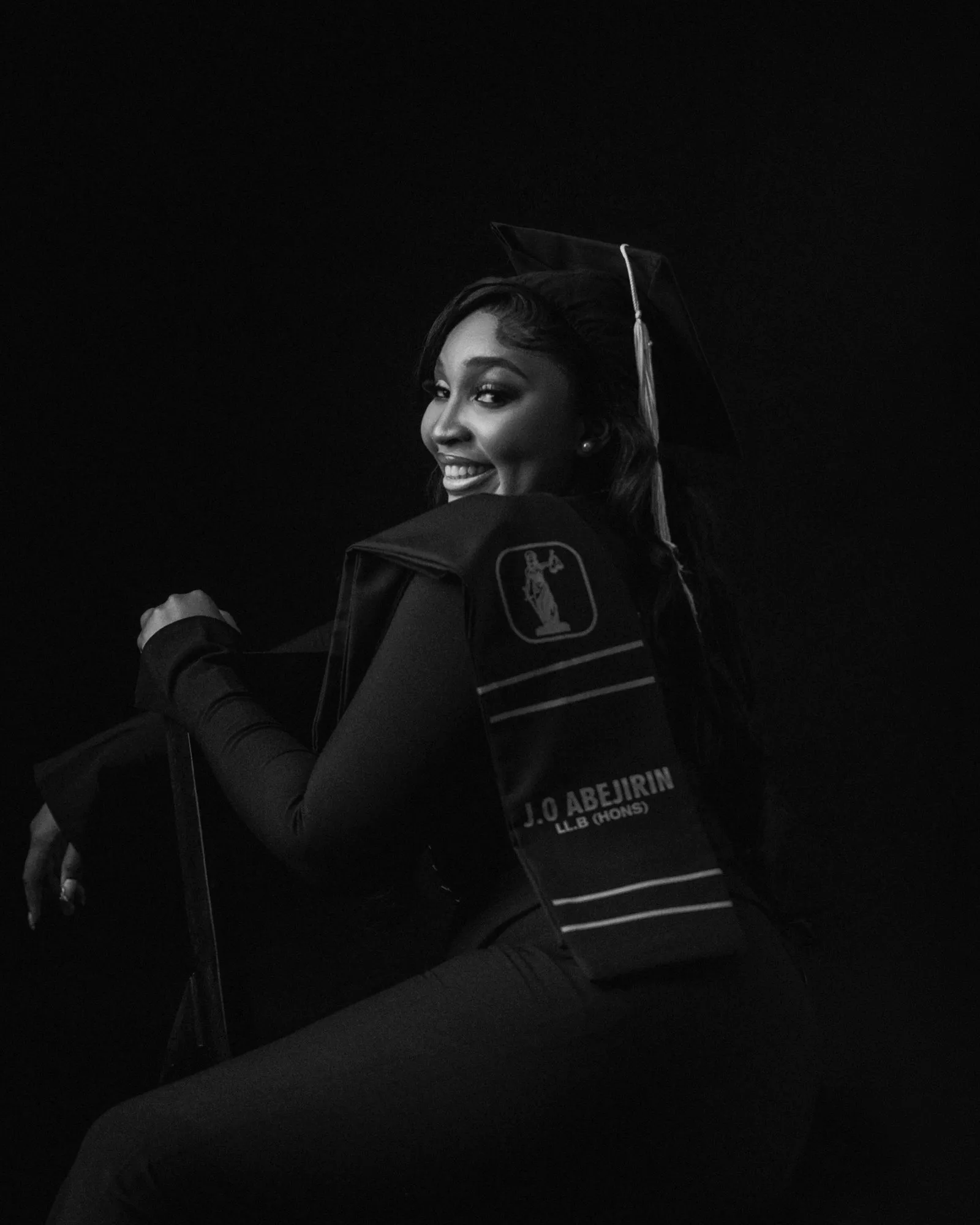 Graduate seated in black with her stole, in low dramatic light