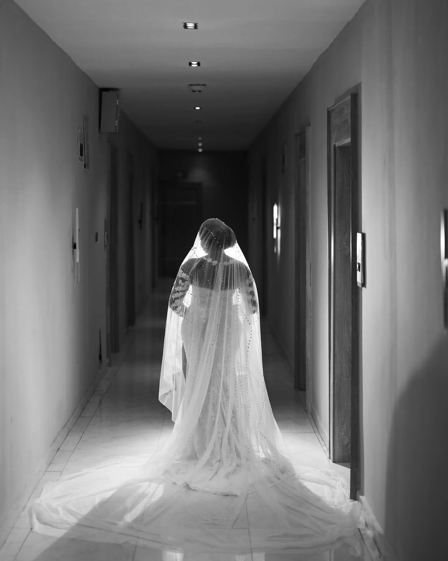 Black-and-white photo of the bride walking down a corridor, her veil trailing behind
