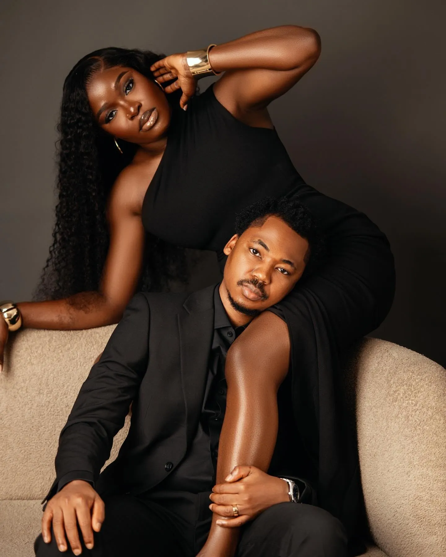 Couple in black, she leans across him on a cream sofa