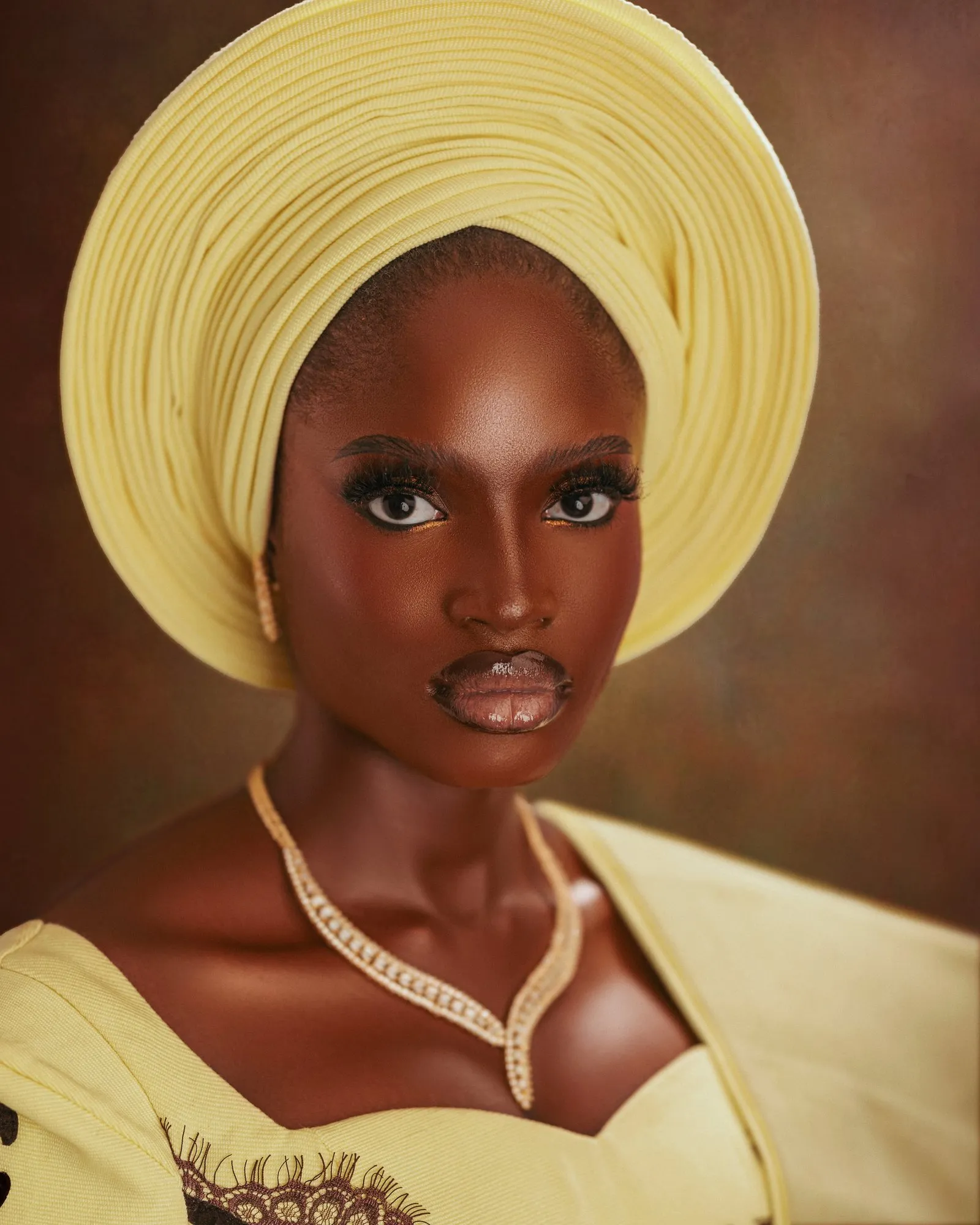 Close portrait of the bride in a butter-yellow gele and pearl necklace