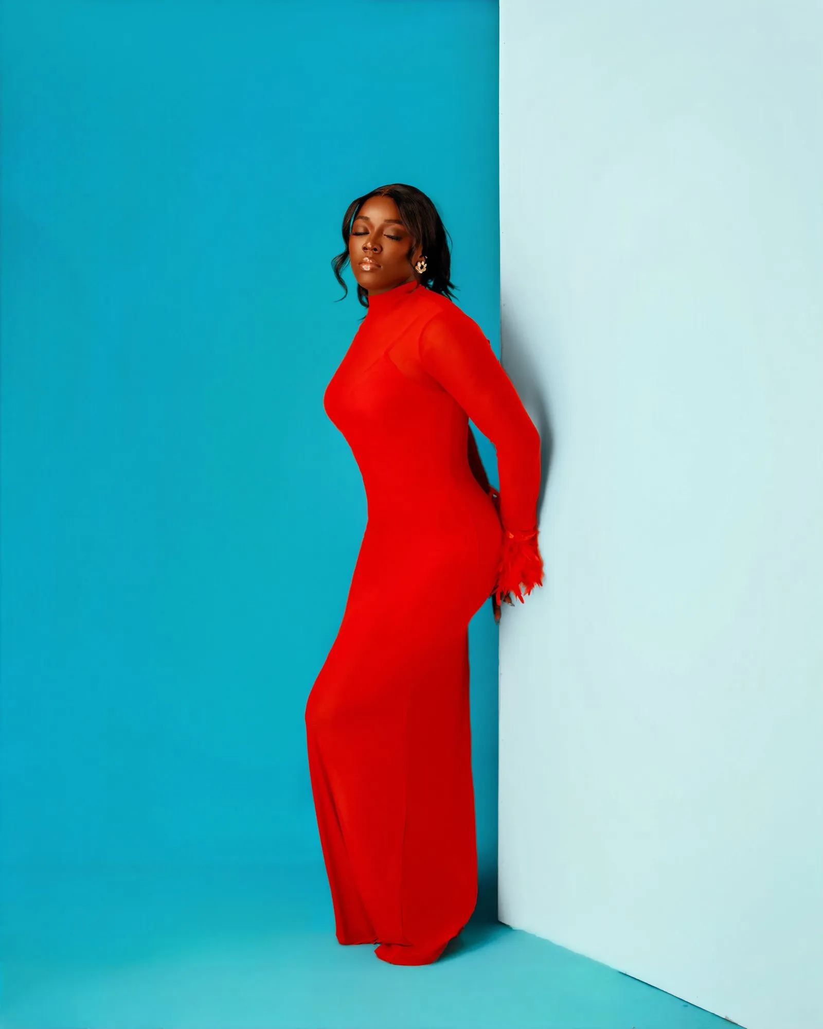 Woman in red leaning against a white wall on the teal set