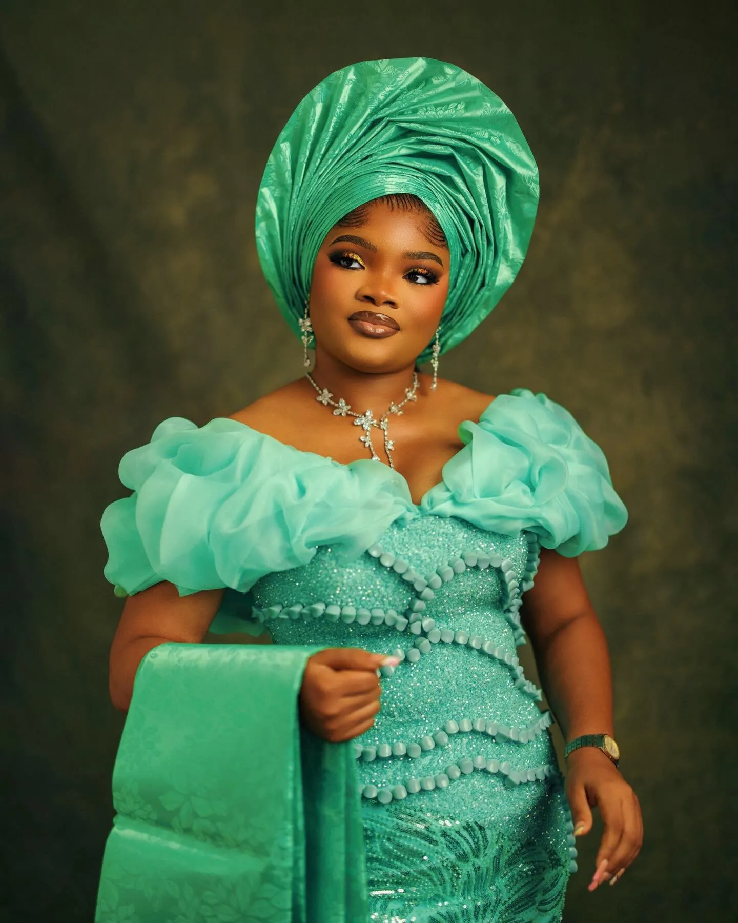 Woman in jade holding a folded aso-oke fan