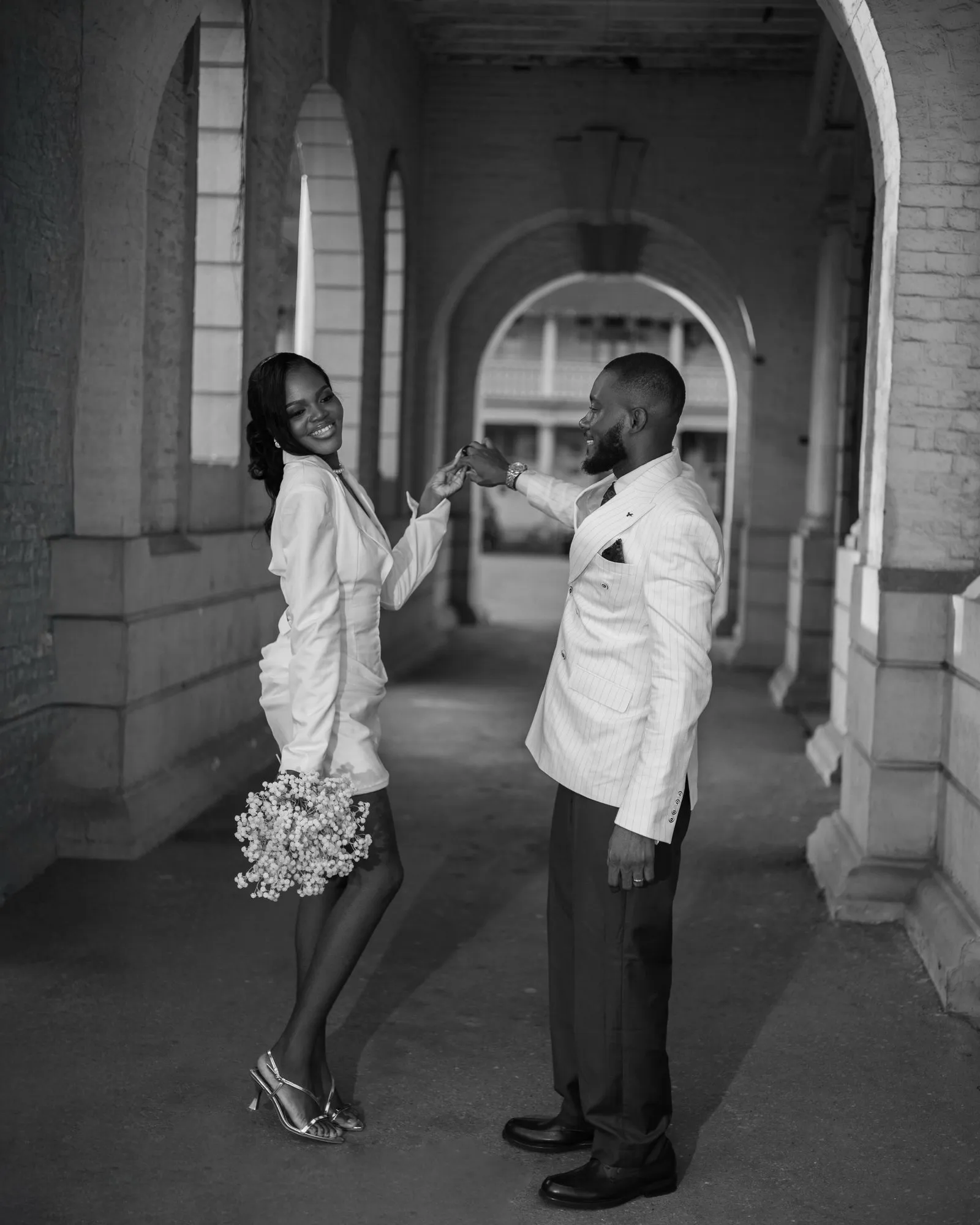 Black-and-white photo of the couple in an arcade, bride holding her bouquet