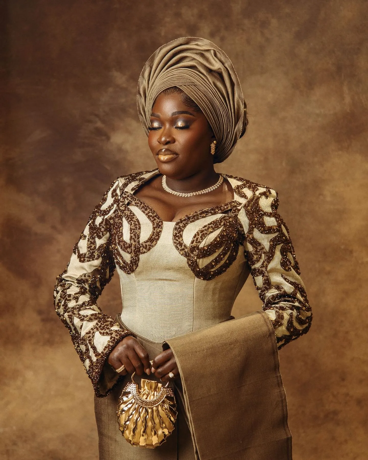 Bride in a brown gele and cream-and-brown appliqué, holding a beaded purse