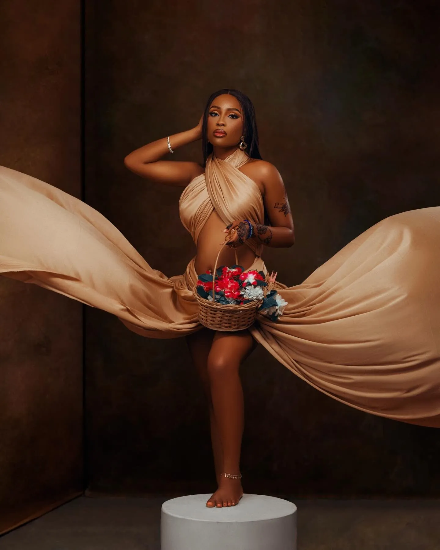 Woman standing on a plinth holding a basket of red flowers, caramel silk flying out on both sides