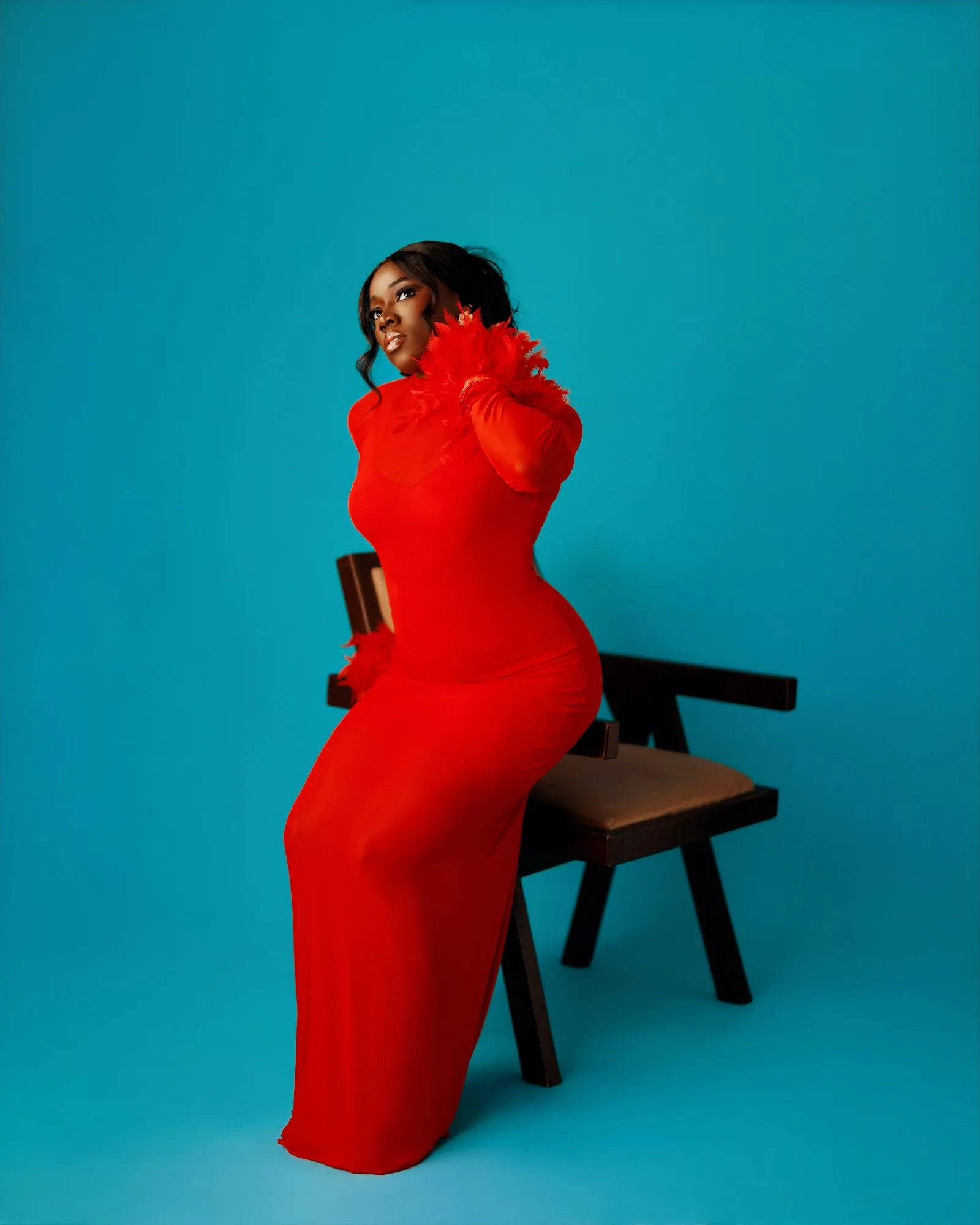 Woman in red seated, hand lifted to her hair