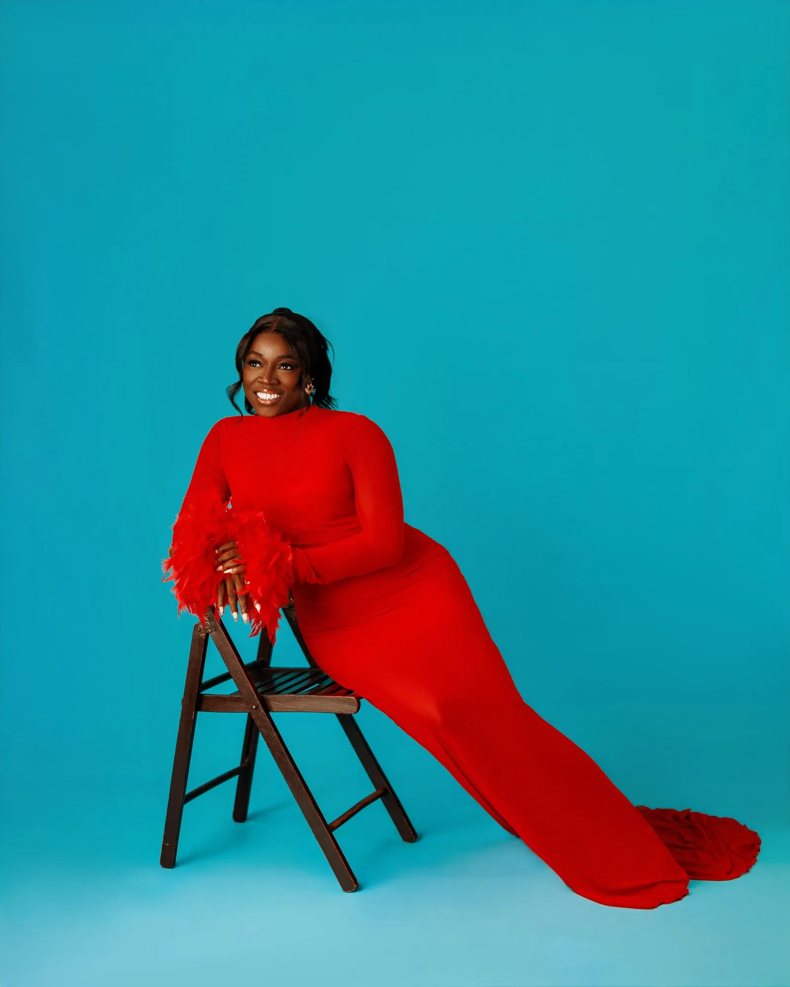 Woman reclining on a chair with her red train spread across the floor