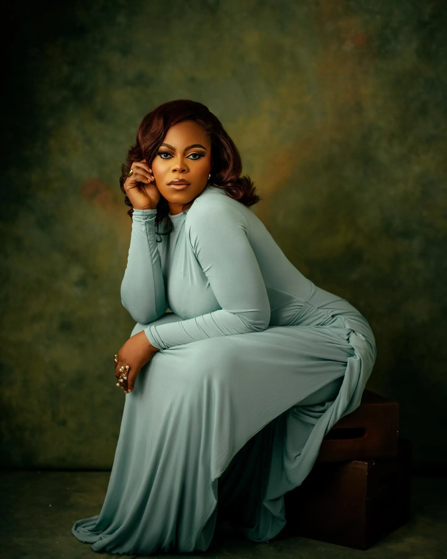 Woman seated on a box, sage dress draped to the floor