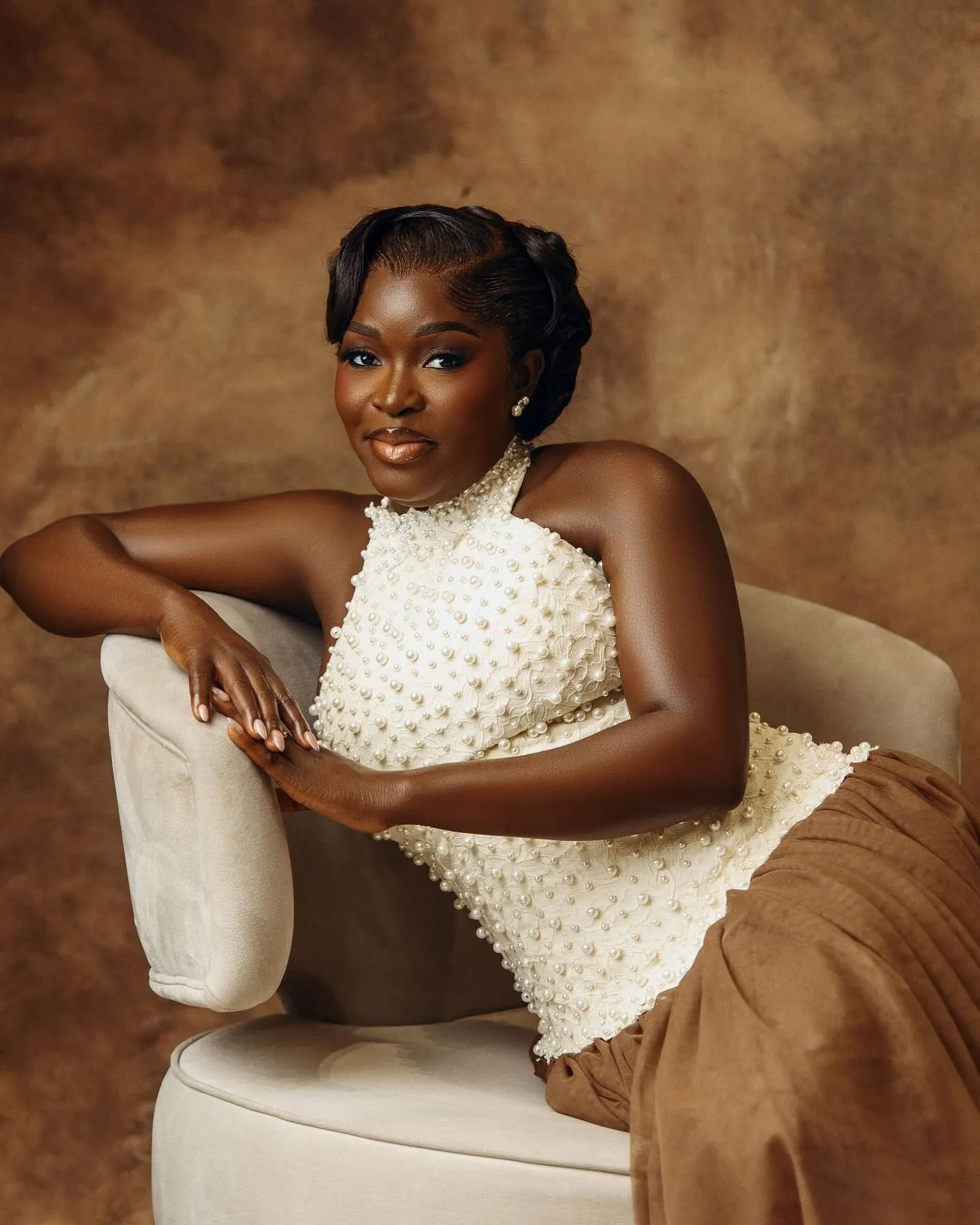 Bride in a pearl-beaded halter top, seated in a cream armchair