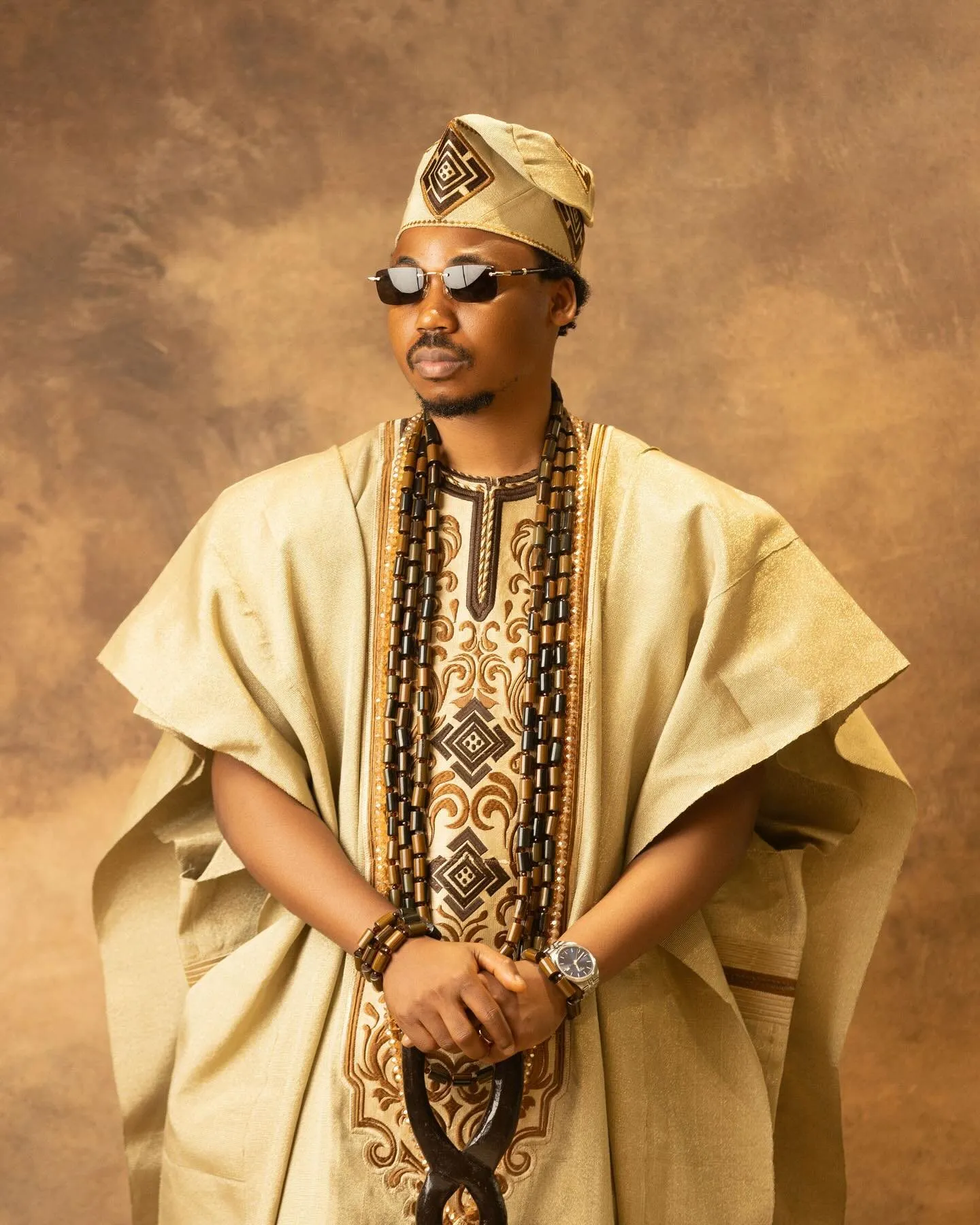 Groom in a gold agbada with sunglasses and a carved cane